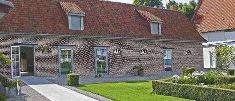 A brick building with a tiled roof, a paved entrance, and a well-maintained lawn.