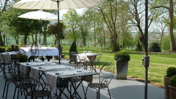 Un espace de restauration en plein air, avec des tables et des chaises, entouré d’arbres et d’un paysage verdoyant.