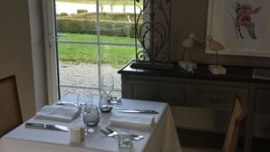 Une table à manger dressée avec de la vaisselle, une lampe et un tableau représentant des fleurs.