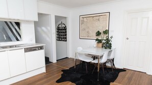 A modern kitchen with white cabinets, a dining area with a white table and chairs, a black leather rug, and a framed map on the wall.