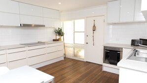 A modern kitchen with white cabinetry, a stainless steel range hood, and a built-in oven.