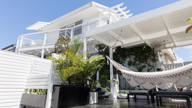 A modern outdoor patio area with a white railing, a hammock, and potted plants.