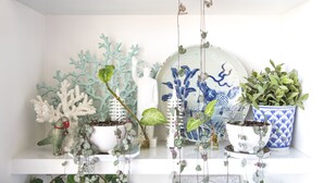 A shelf with various potted plants, decorative items, and a white bird figurine.