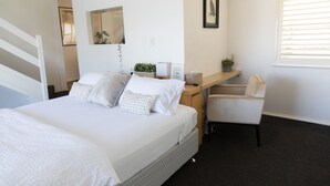 A bedroom with a bed, a desk, a chair, a mirror, and a window.