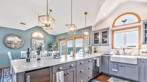 A modern kitchen with a large island, pendant lights, and a view of the outdoors.
