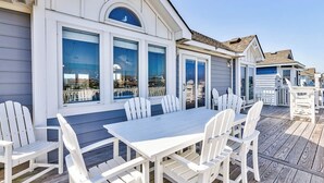A white wooden deck with a white table and chairs, overlooking a body of water.