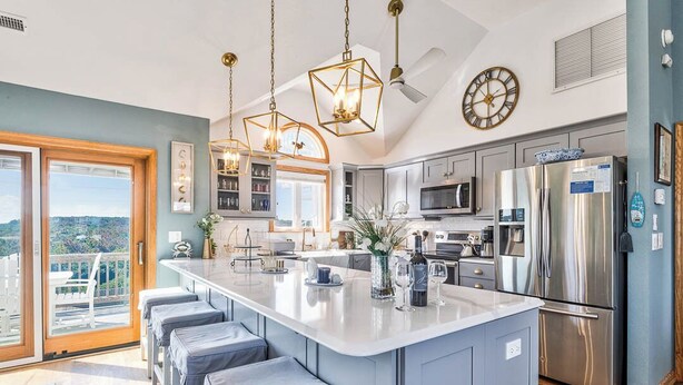 A modern kitchen with a central island, stainless steel appliances, and a large window overlooking a balcony.