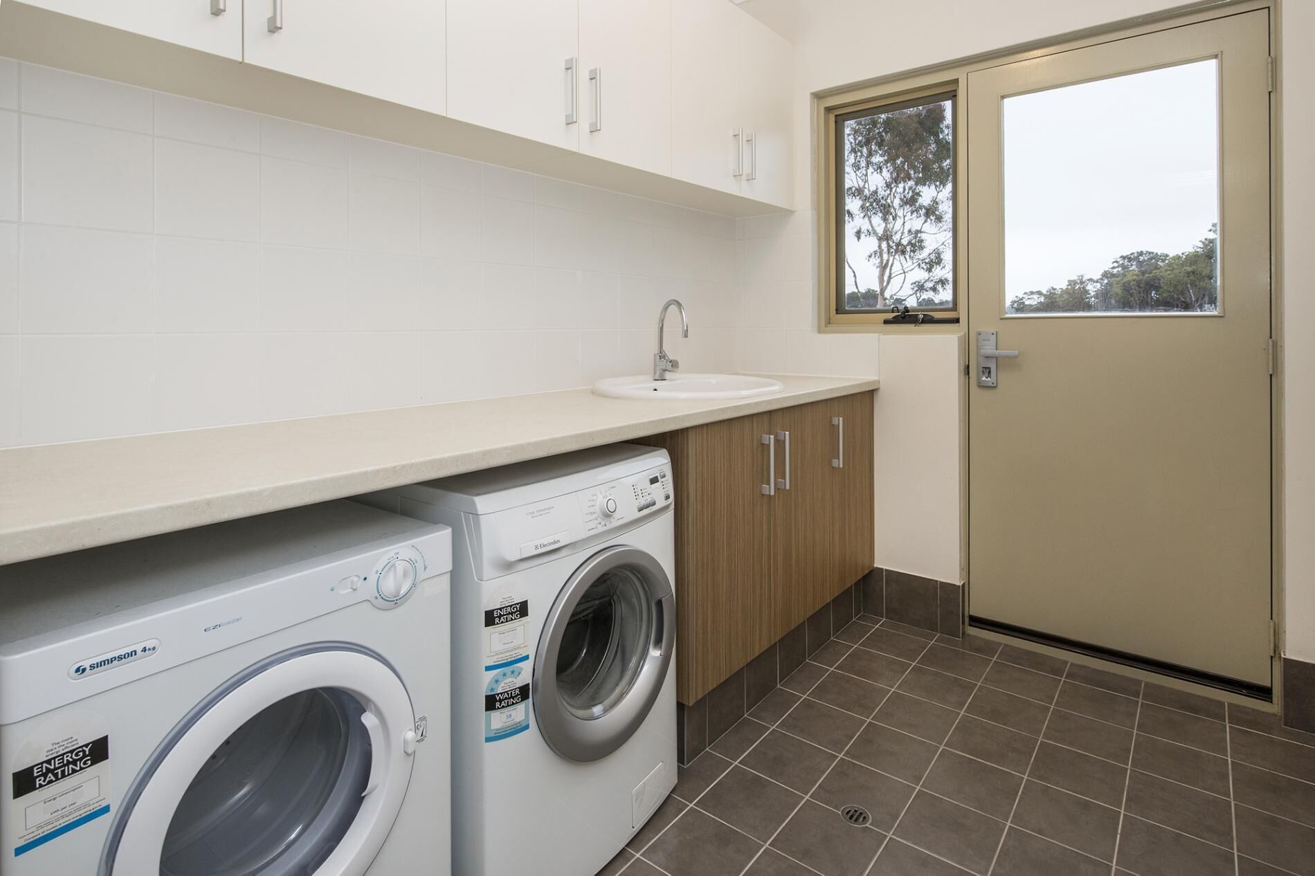 A laundry room with a front-loading washing machine and dryer, a sink, and a door with a window.