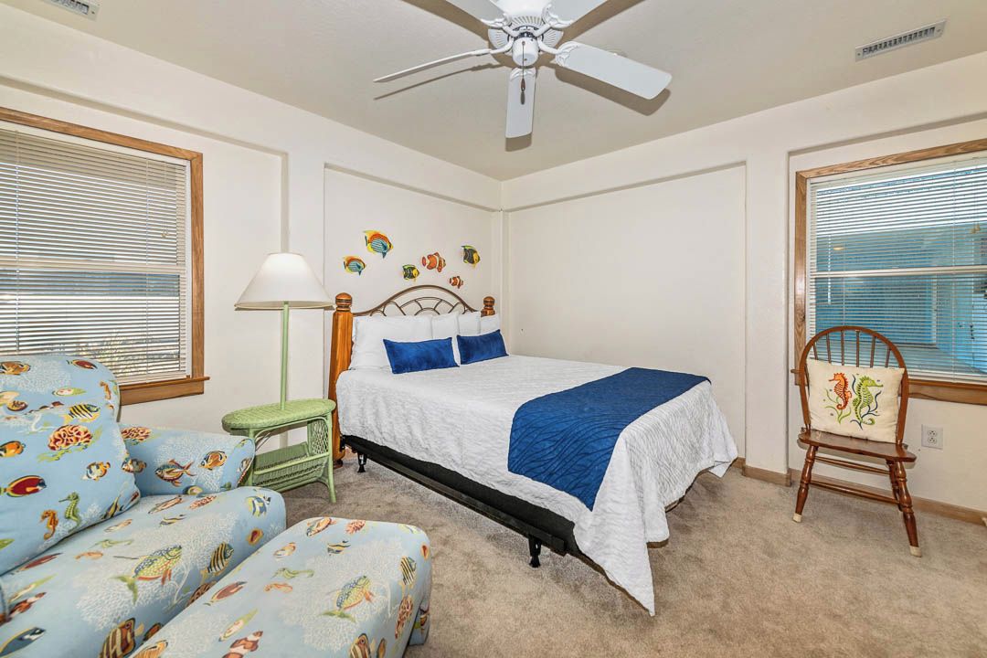 A bedroom with a bed, a chair, a nightstand, a lamp, and a ceiling fan.