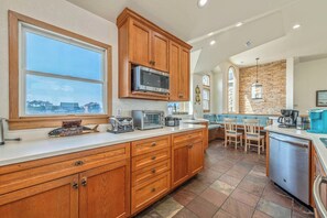 A kitchen with wooden cabinets, a microwave, and a large window. - The Lodge | Oceanfront | Private Pool, Hot Tub | Nags Head (Nags Head)