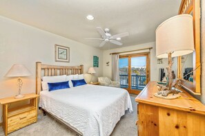 A bedroom with a bed, nightstands, a ceiling fan, a window with a view, and a wooden dresser. - The Lodge | Oceanfront | Private Pool, Hot Tub | Nags Head (Nags Head)