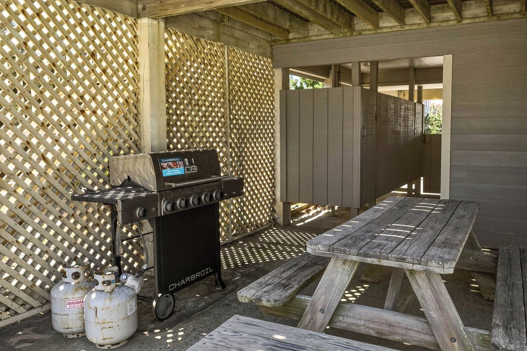 Un espace barbecue extérieur comprenant un gril, deux bouteilles de propane et une table de pique-nique en bois.