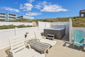 An outdoor patio with white chairs, a wooden table, and a hot tub. - The Lodge | Oceanfront | Private Pool, Hot Tub | Nags Head (Nags Head)