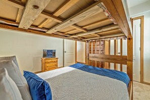 Un dormitorio con techo de madera, una cama con ropa de cama azul, un aparador de madera y una puerta.