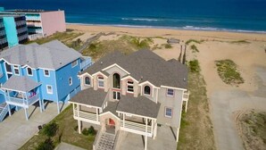 A beachfront property with a large house, a smaller attached structure, and a blue building. - The Lodge | Oceanfront | Private Pool, Hot Tub | Nags Head (Nags Head)