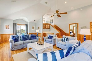 A spacious living room with a high ceiling, a ceiling fan, and a staircase leading to an upper level. - Corolla Crush | 485 ft from the beach | Private Pool, Hot Tub | Corolla (Corolla)