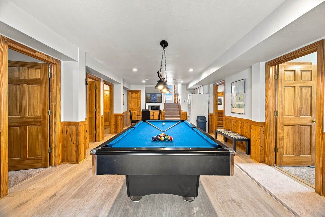 A pool table in a hallway with wooden doors and a staircase in the background.