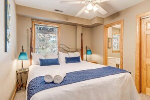 A neatly made bed with white and blue bedding, two bedside lamps, a ceiling fan, and a window with a view of greenery. - Corolla Crush | 485 ft from the beach | Private Pool, Hot Tub | Corolla (Corolla)