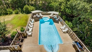 Une piscine extérieure dotée de chaises longues et de parasols, entourée d’une terrasse en bois et d’une végétation luxuriante.