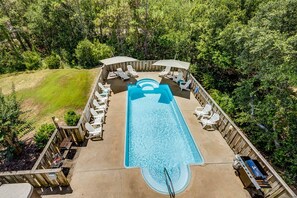 An outdoor swimming pool with lounge chairs and umbrellas, surrounded by a wooden deck and lush greenery. - Corolla Crush | 485 ft from the beach | Private Pool, Hot Tub | Corolla (Corolla)