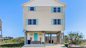 A two-story house with a porch, a blue door, and a satellite dish. - Sandpiper's Paradise | Oceanfront | Hot Tub | Kill Devil Hills (Kill Devil Hills)