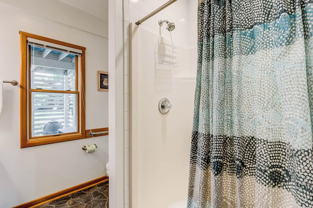 A bathroom with a shower, a window with blinds, and a patterned shower curtain.