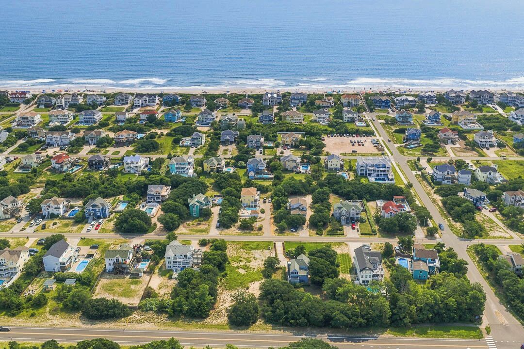 A coastal residential area with houses arranged in a grid pattern, a road in the foreground, and the ocean in the background.