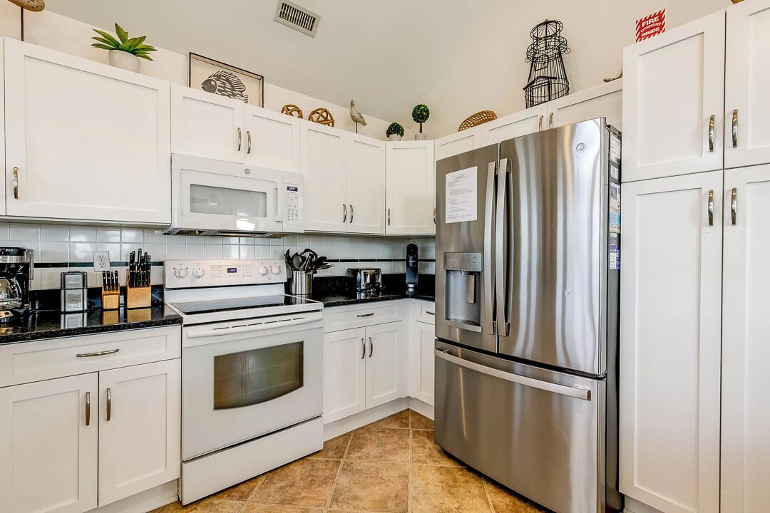 A modern kitchen with white cabinets, a stainless steel refrigerator, a microwave, and an oven.
