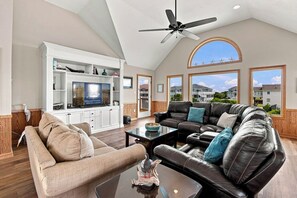 Un salon spacieux avec un plafond haut, un ventilateur de plafond, une grande fenêtre offrant une belle vue et une cheminée.