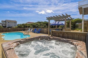 Un jardin avec un jacuzzi, une piscine et une pergola en bois.