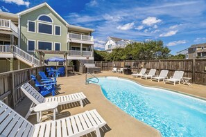 Une piscine avec des chaises longues, une terrasse en bois et un immeuble à plusieurs étages doté de balcons.