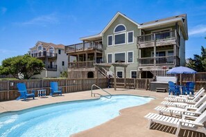 A pool area with a wooden deck, lounge chairs, and a barbecue setup.