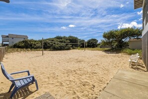 Un espace extérieur sablonneux avec un filet de volley-ball, une chaise bleue et une terrasse en béton.