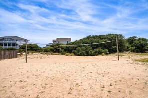 A sandy beach with a volleyball net, a wooden fence, and houses in the background.