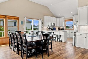Une cuisine spacieuse dotée d’un grand îlot central, de meubles blancs et d’un coin repas avec des chaises en bois foncé.
