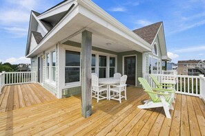 A wooden deck with a covered patio area, a white table with chairs, and a green Adirondack chair.