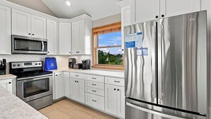 A modern kitchen with white cabinets, stainless steel appliances, and a window with a view. - Legacy | 980 ft from the beach | Dog Friendly, Private Pool, Hot Tub | Corolla (Corolla)
