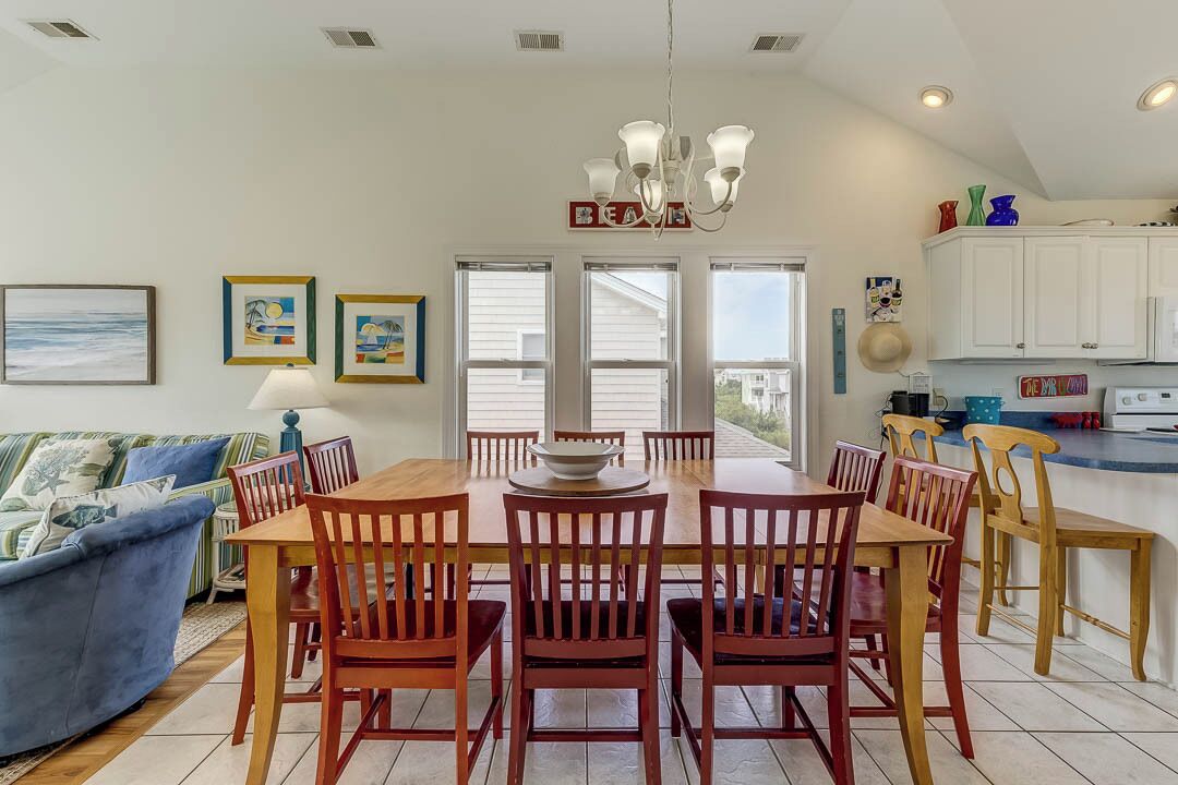 A dining area with a wooden table and chairs, a chandelier, and a view of the outdoors through large windows.