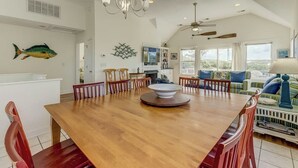 Une salle à manger spacieuse, avec une table et des chaises en bois, un lustre et une vue sur l’extérieur grâce à de grandes fenêtres.