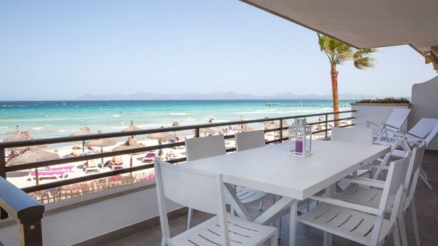 Una terraza con una mesa y sillas que da a una playa con sombrillas y gente.
