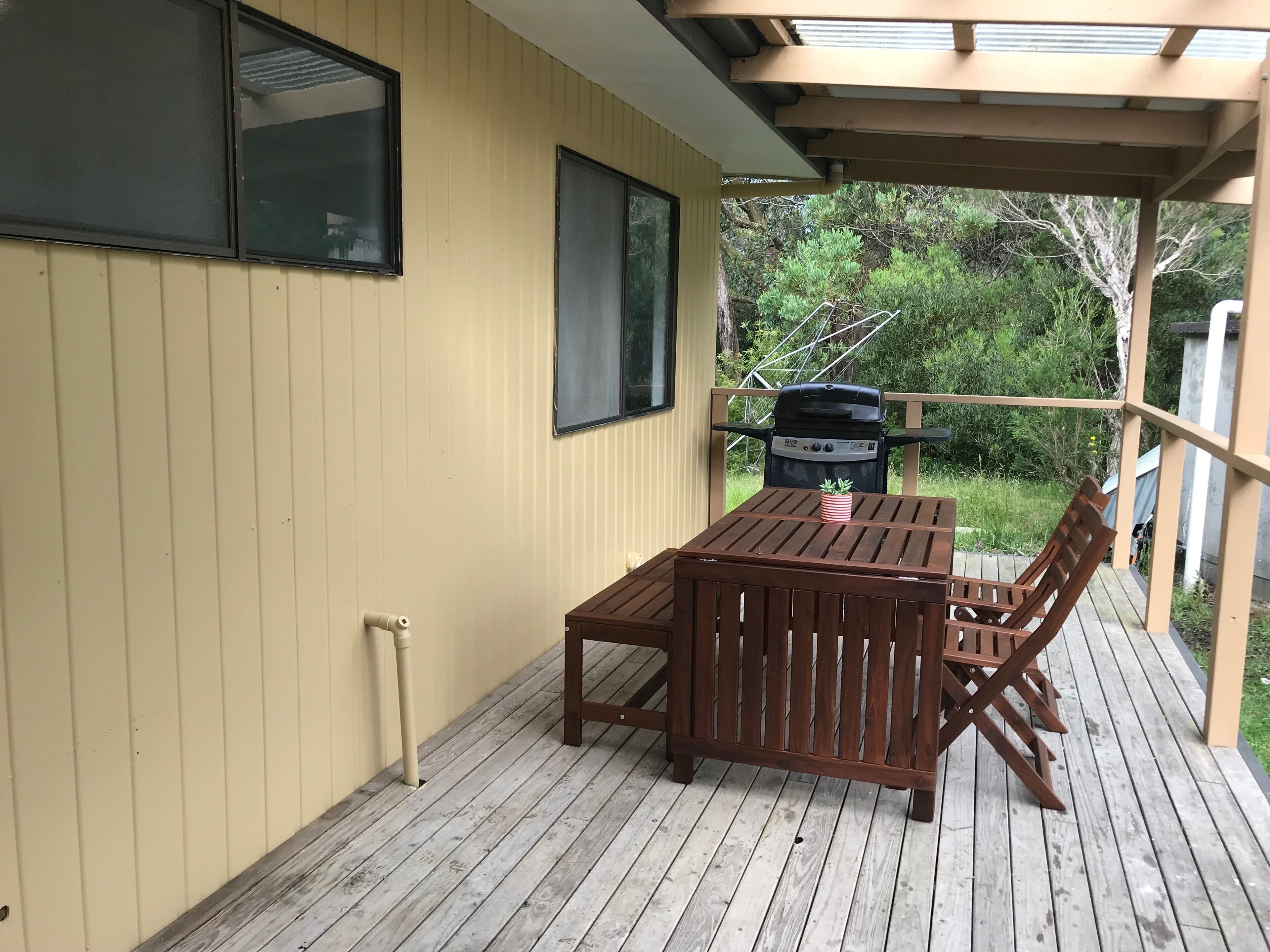 Une terrasse en bois avec une table et des chaises, un barbecue et une fenêtre.