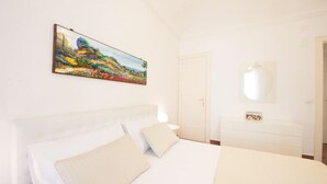 Een slaapkamer met een bed, nachtkastje, dressoir, spiegel en een schilderij aan de muur.