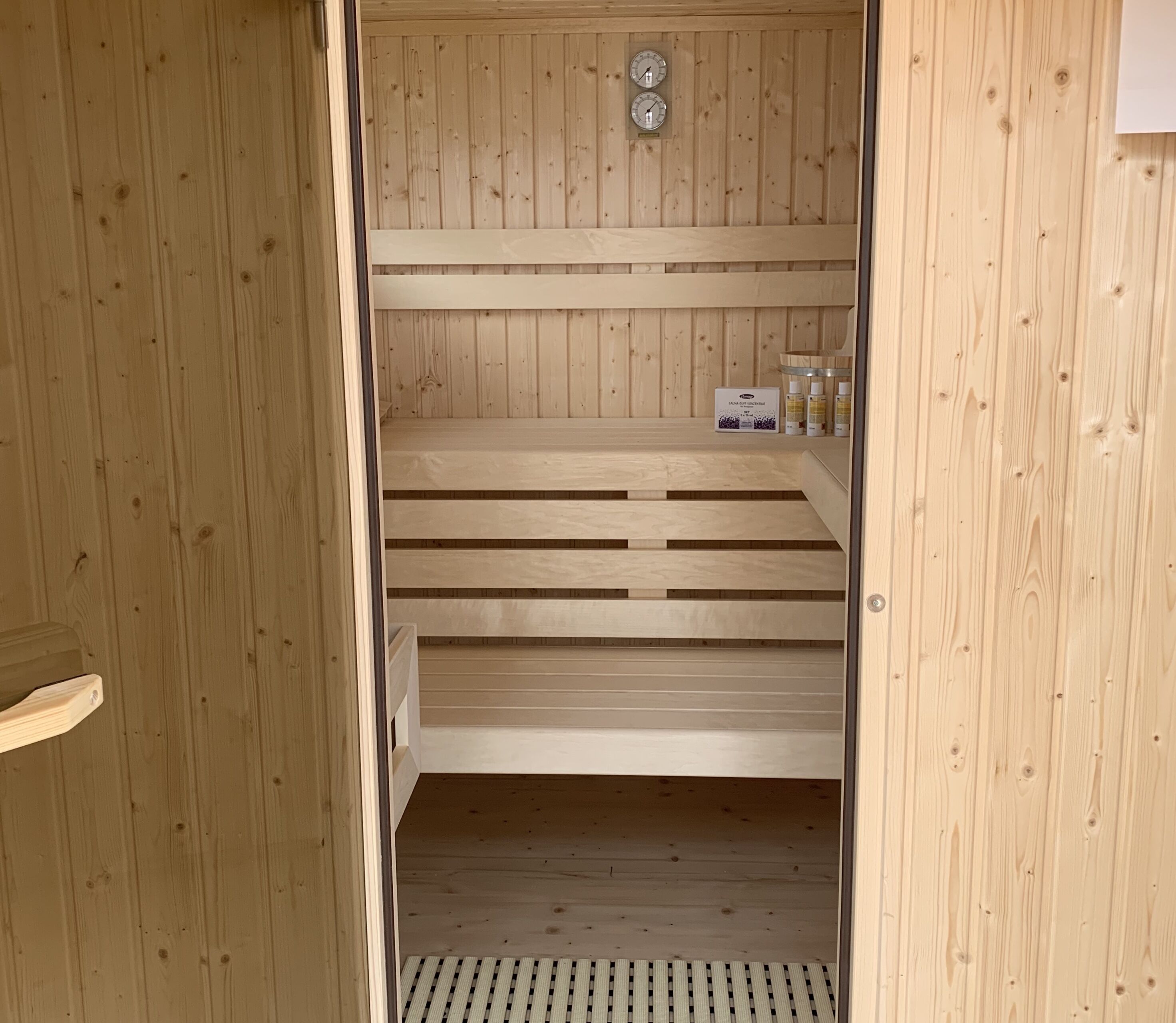 Eine Sauna mit Holzwänden und -bänken, einem Belüftungssystem und einer Reihe abgefüllter Produkte auf der Bank.