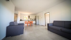 A modern living room with a sofa and chairs, a dining area with a table and chairs, and a kitchen in the background.