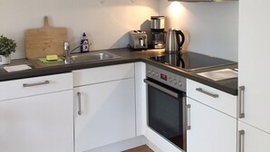 Una cocina compacta con armarios blancos, encimera negra, tostadora, tetera y tabla de cortar de madera.