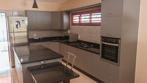 Une cuisine moderne avec des meubles gris, un réfrigérateur en acier inoxydable, une cuisinière à gaz et un four encastré.