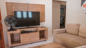 Un salon avec un téléviseur à écran plat posé sur un meuble en bois, un ventilateur, un canapé et une table basse.