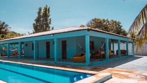Un espace aménagé au bord de la piscine, avec un bâtiment aux couleurs turquoises, une piscine et des sièges extérieurs.