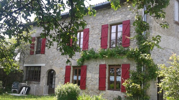 A stone building with red shutters, a grassy yard, and outdoor seating.