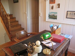 A wooden desk with a laptop, a green desk lamp, a brass lamp, and a red gift box.